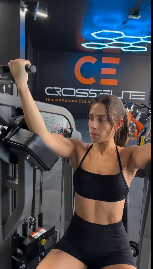 Socia entrenando bíceps en la Nautilus Nitro Biceps Curl, con el logotipo de CrossElite al fondo